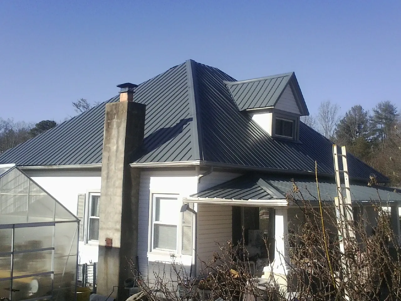 Dark blue standing seam metal roof on a white farmhouse with dormer — Slate & Tile Roof Repair by Roofing Brothers in Blackstone